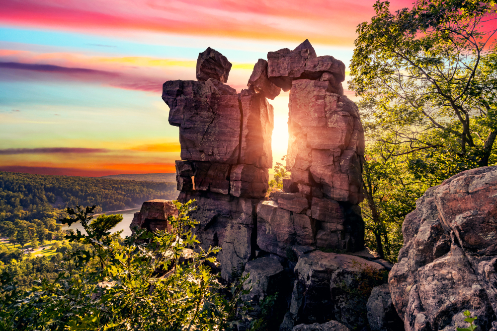 sunset seen through a rock formation in Devils Lake State Park. The lake is in the background and there are trees around.  