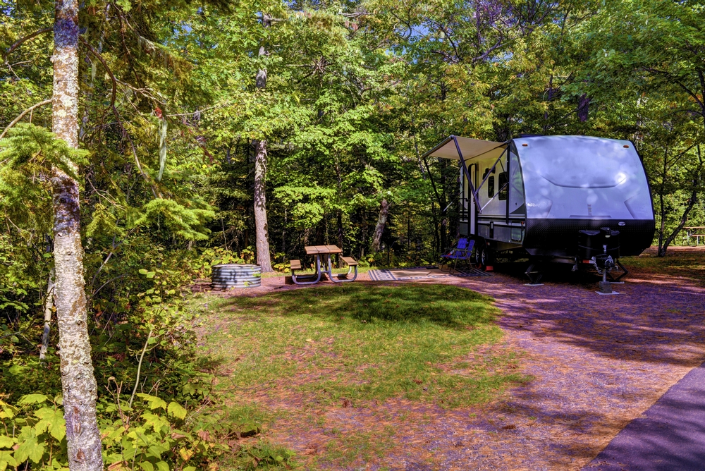 An RV in a site that has a fire pit, picnic table, and is surrounded by trees. 