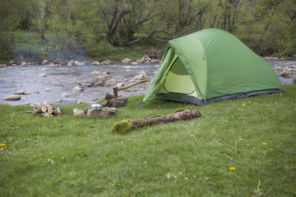 A green tent on the shore of a river in a grassy field. 