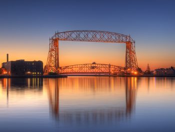 metal lift bridge at dusk with orange yellow sky and reflection on still water