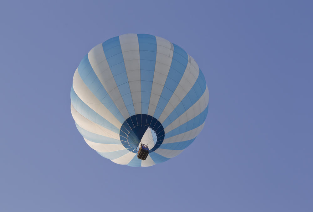 Blue and white stripped hot air balloon in the blue sky taken from below, This is one of the things to do in Lake Geneva 