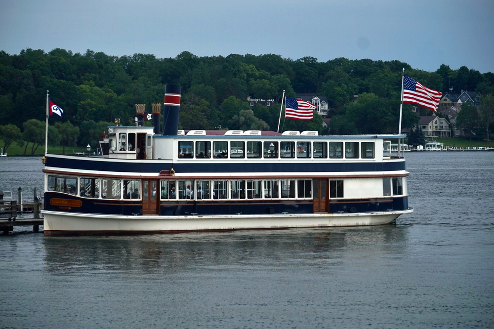 A old style double decker boat docked in the water with two American flags flying. 