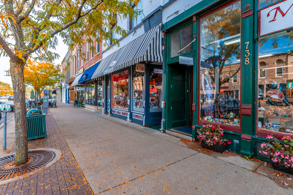 Downtown city with green stores with large glass storefronts, brick walkway in foreground. Downtown Lake Geneva.