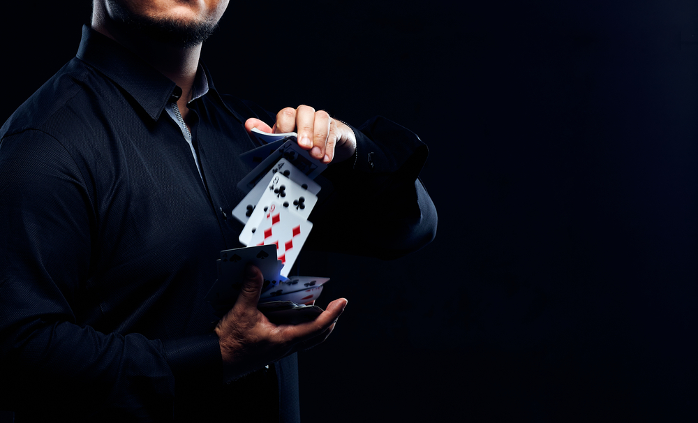 Man in a dark shirt on a dark background with cards been shuffled between his hands. 