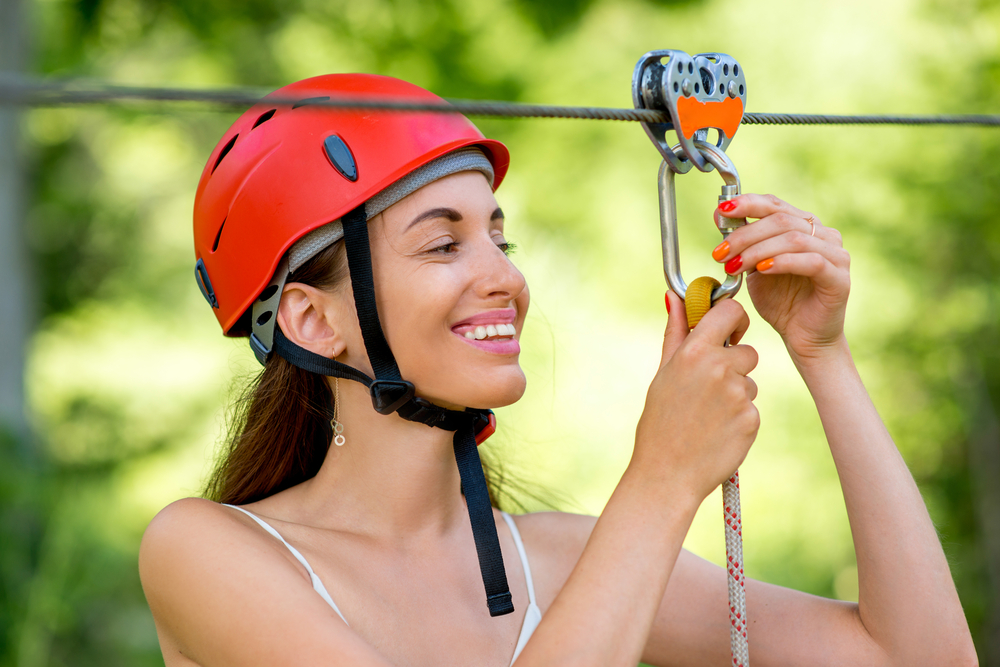 A female on a zip wire wearig a crash helmet. Trees are in the background and its a close up photo 