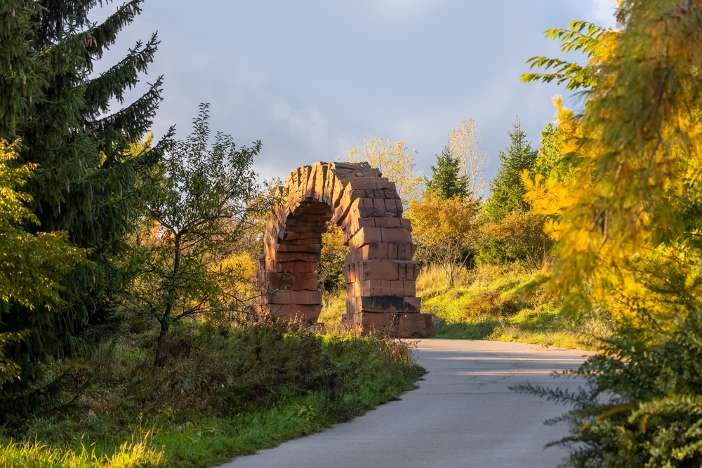 A trail with a stone arch surrounded by trees in the Frederik Meijer Gardens And Sculpture Park, one of the best things to do in Grand Rapids. 