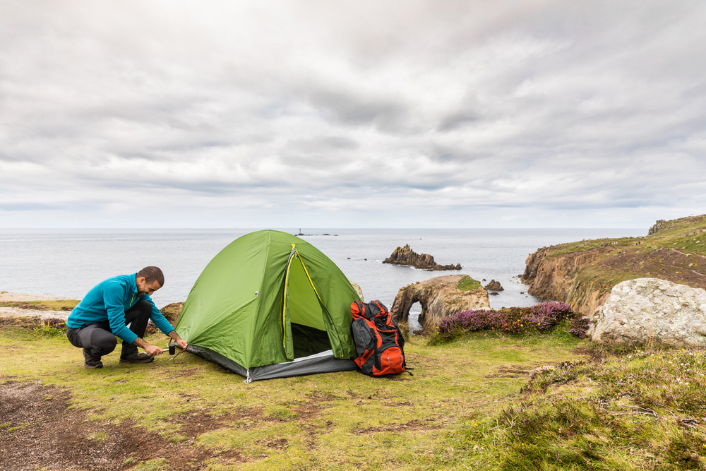 A man setting up a green tent on top of a rocky lakeshore