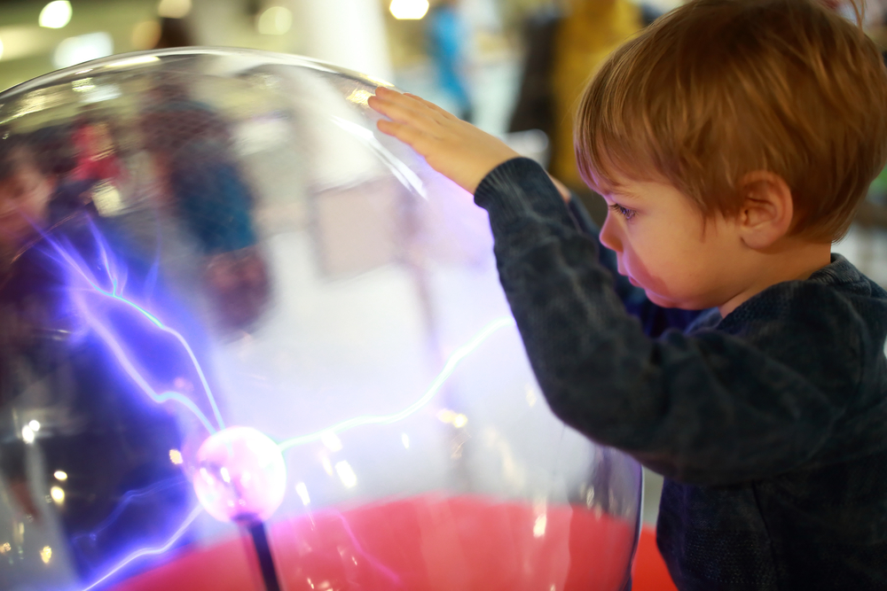 A kid looking into a big glass globe that has electrical currents running through it at a children's museum. 