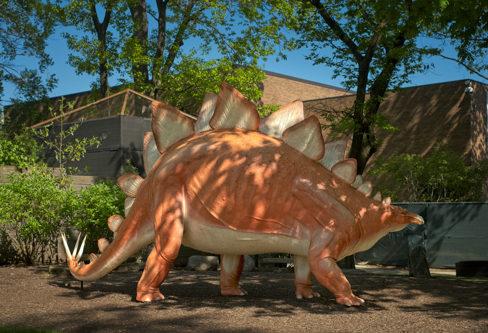 A large sculpture of an orange dinosaur outside of a museum. 