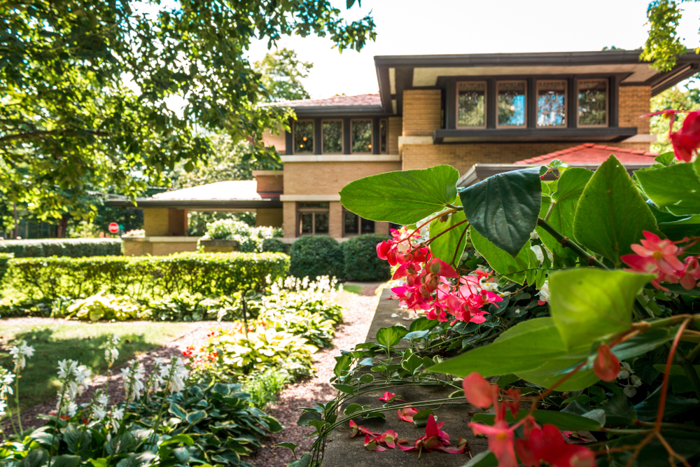 The exterior of a Frank Lloyd Wright designed house with red and white flowers around it. It's one of the best things to do in Grand Rapids