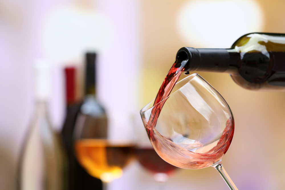 Red wine being poured into a glass with bottels in the background in an article about wineries in Indiana  