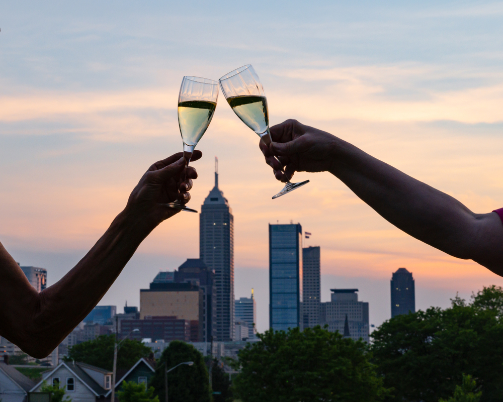 Two people toasted with white wine with the Indianapolis skyline in the background in an article about wineries in Indiana  
