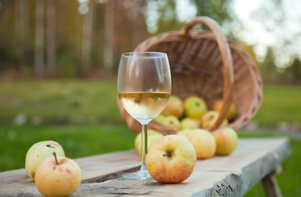 apple cider in a chilled wine glass, rustic settings with apples and wicker basket in an article about wineries in Michigan