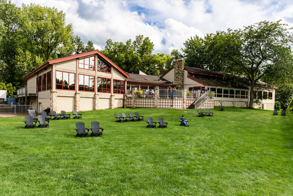  The Tabor Hill Winery & Restaurant is a small and relaxing property featuring plenty of wine, food, and a beautiful vineyard for guests to walk around. Here you see a grass bank with chairs and a building in the background. In an article about wineries in Michigan. 