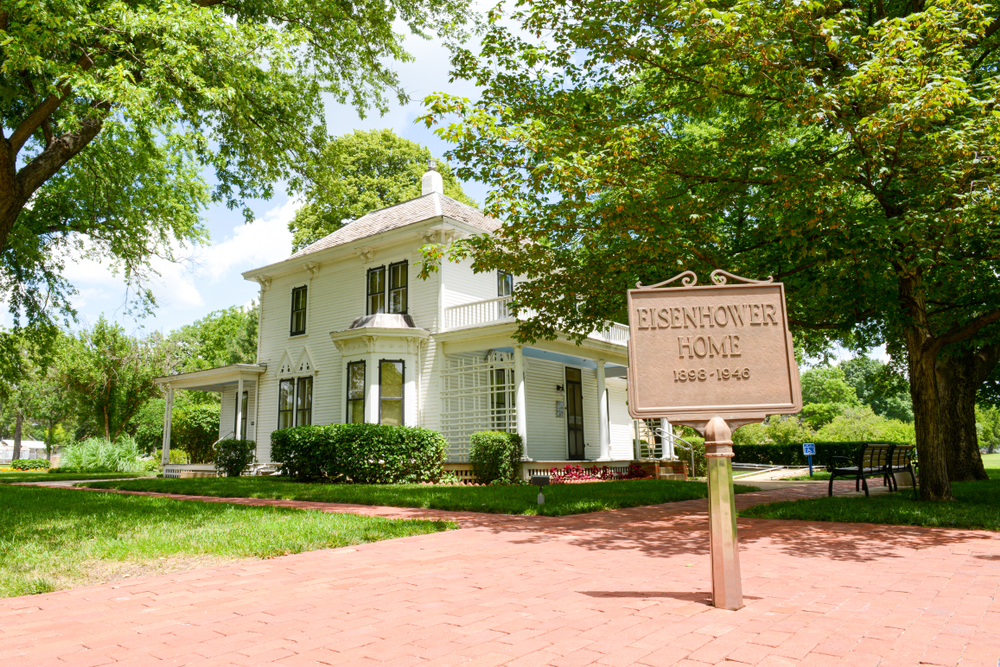 beige colored historic house with official sign in front surrounded by green trees and manicured law, small towns in Kansas