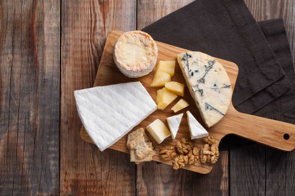 Flat lay image of a cheese board with multiple cheeses and walnuts.