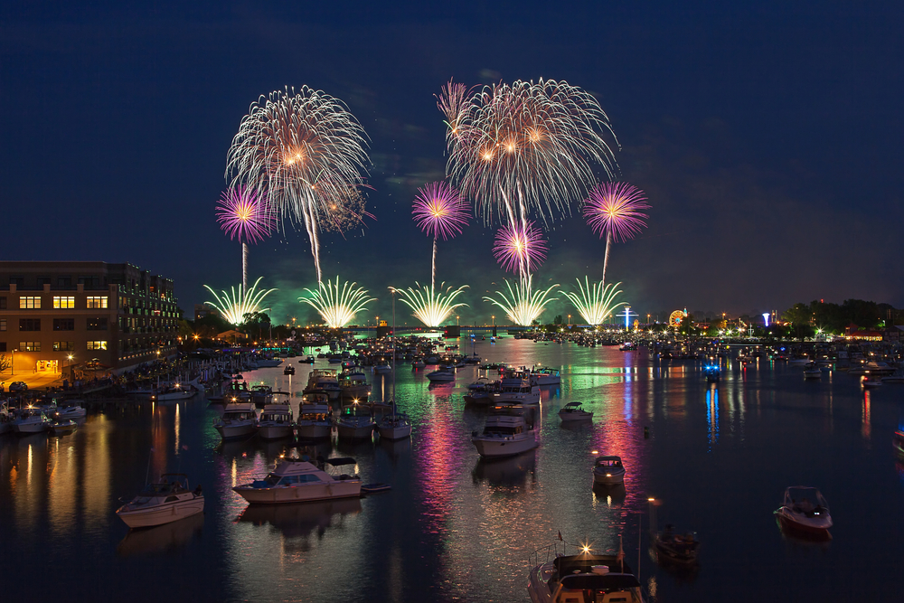 Fireworks over the river filled with boats and Bay City, MI, at night.