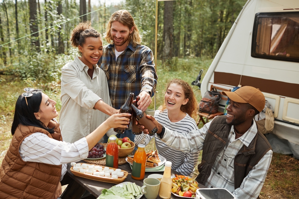 A group of people enjoying a meal and drinks in front of an RV surrounded by the woods, which is perfect for camping in Illinois.