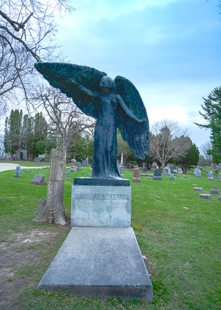 A large black sculpture of an angel spreading her wings on top of a stone  square in the middle of a cemetery in Iowa City. 