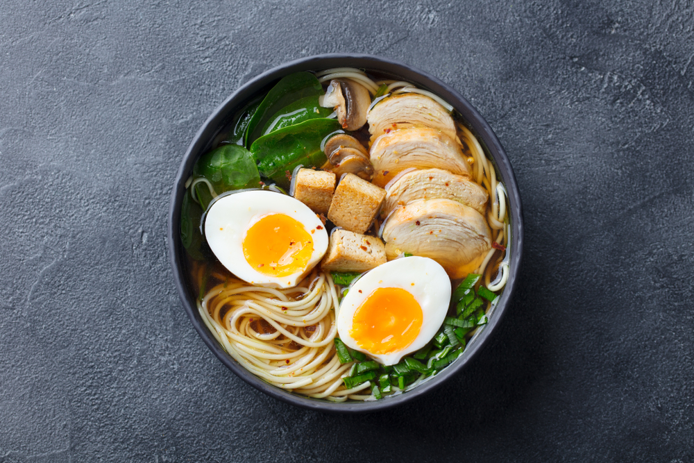 A bowl of Ramen that has two soft boiled eggs, noodles, spinach, tofu, mushrooms, and chicken breast. 