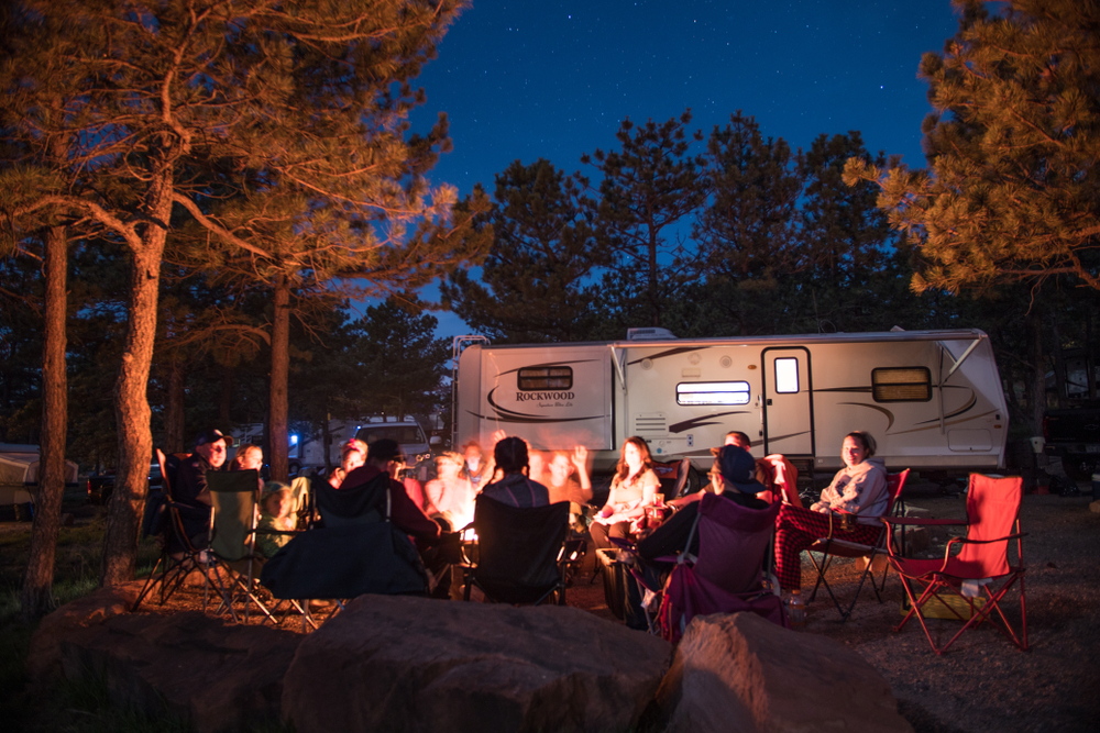 Group sits around campfire under the stars in the summer. The RV is in the background and the fire is in the middle