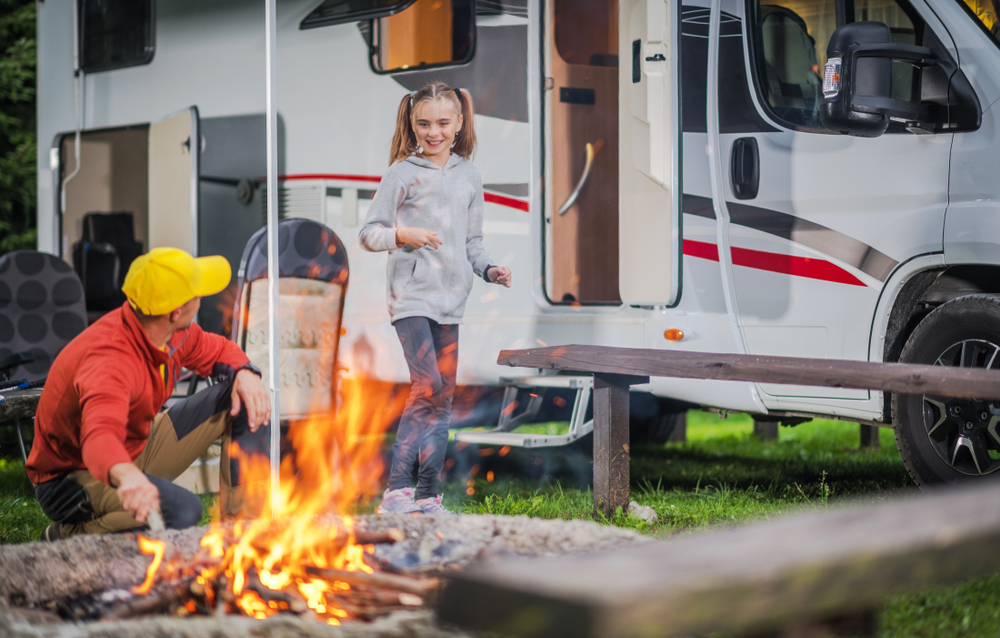 ather with Daughter Having Fun in Front of Campfire. The RV is behind them and there is a fire in the foreground. 
