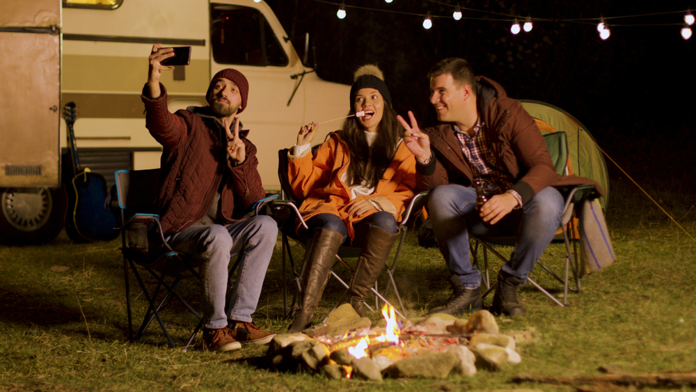 Close friends taking a selfie around camp fire in a cold night . Light bulbs in the background.