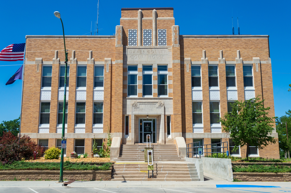 A blonde brick colored historic building with vertical windows , stairs lead up into glass door.. 