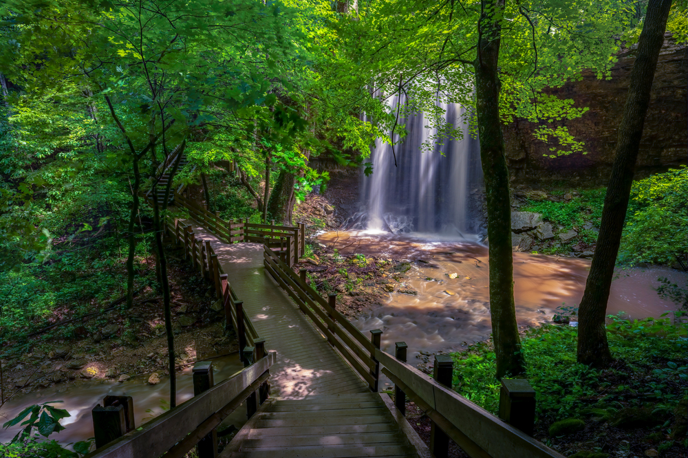 A wooden walkway surrounded by trees  leading down to a large cascading waterfall. 