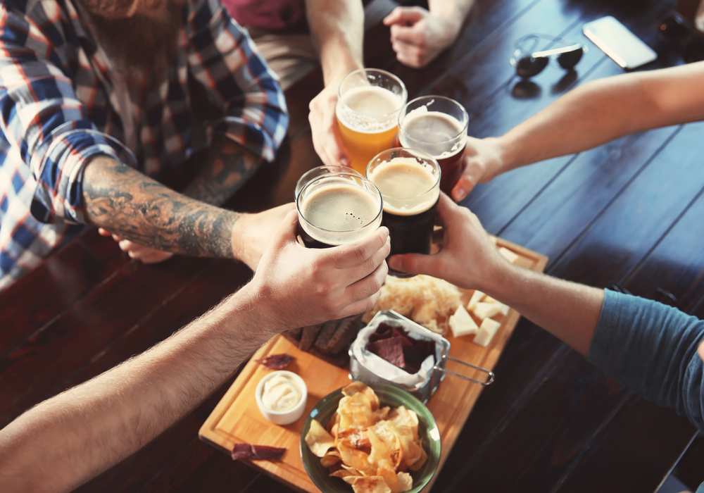 An overhead image of a group of people cheers-ing with craft beers like you can find a breweries in Ohio. They also have snacks on the table. 
