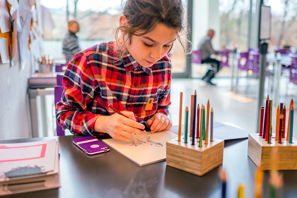 A child drawing in a sketchbook with colored pencils in an art studio in a children's museum. 