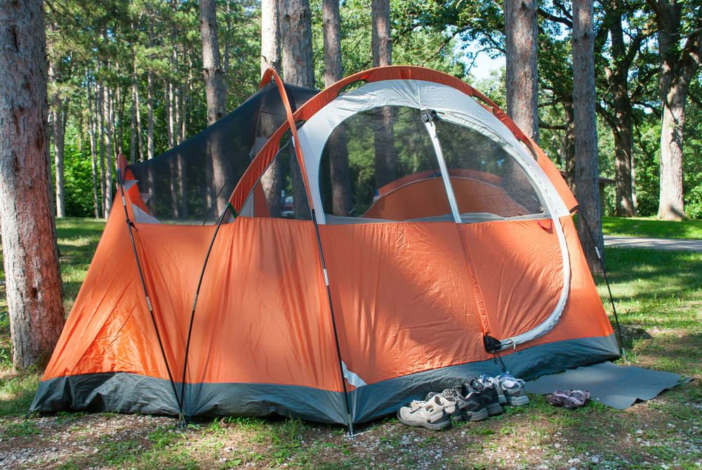 A close up of a large orange tent surrounded by trees near a trail, similar to places to go camping in Illinois. 