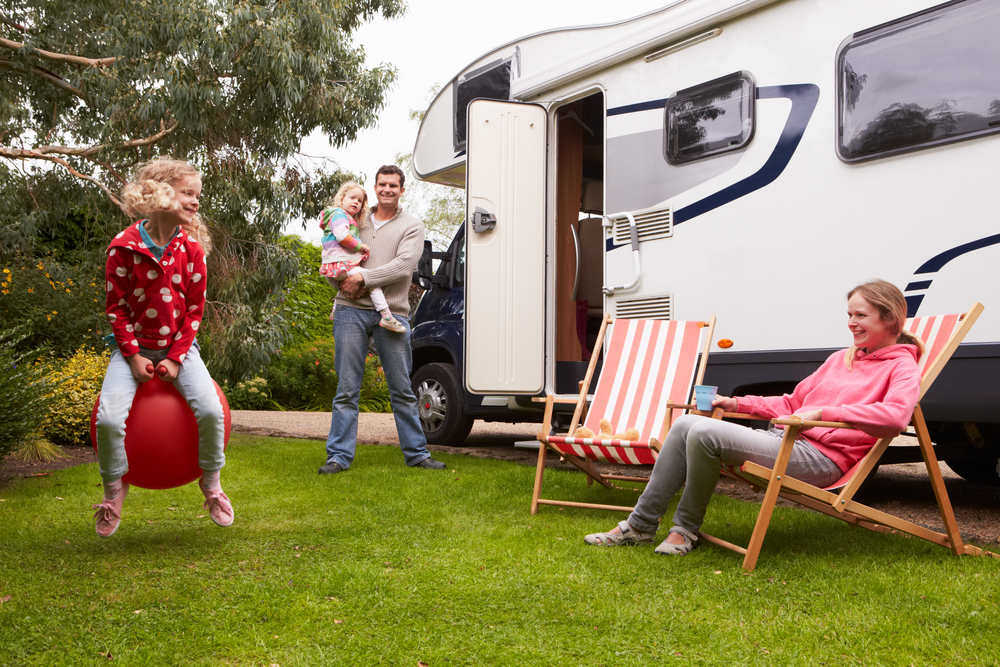 A family with two kids and two adults playing and sitting next to an RV on the grass. 