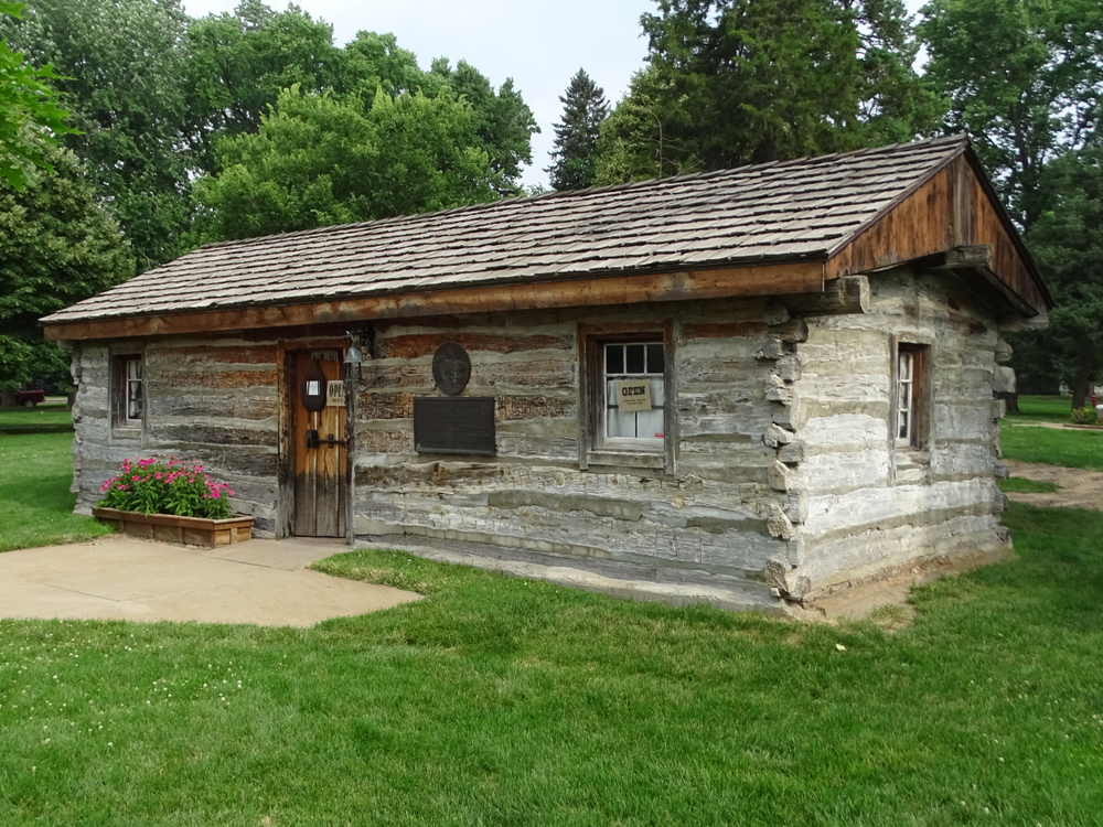 One of the original Pony Express Stations - a brown log cabin with singled roof and flowers next to wooden front door.