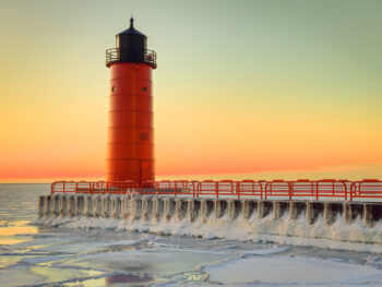 Winter view of red lighthouse with orange sunset in background, one of the lighthouses in Wisconsin