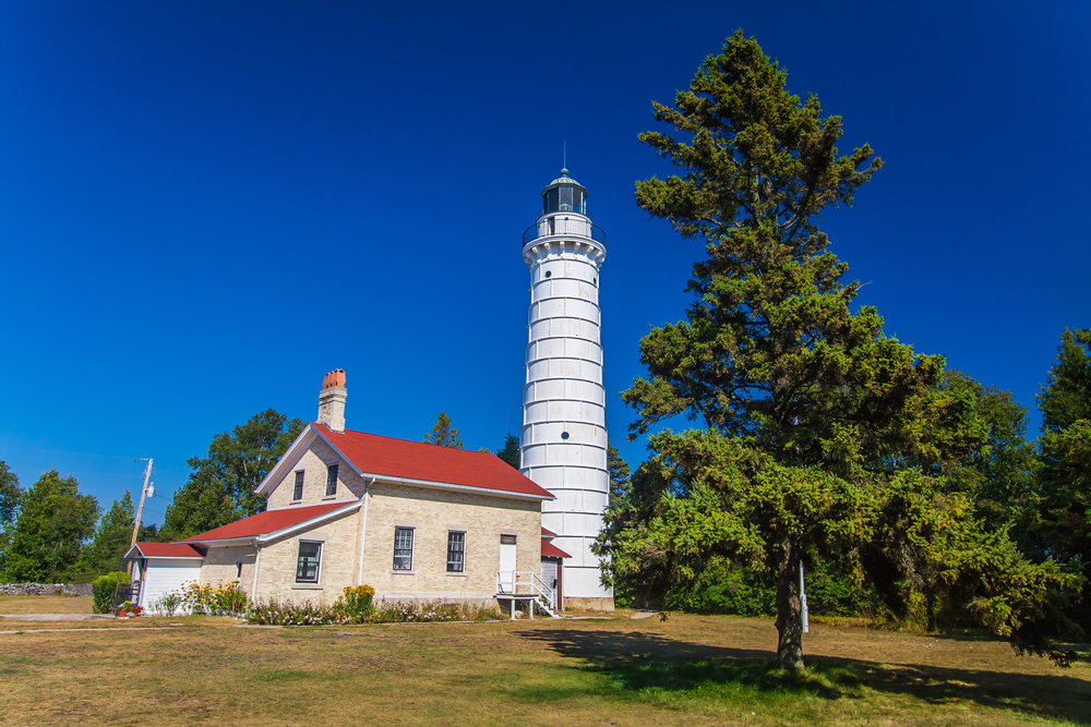 Cana Island Lighthouse in Door County, Wisconsin. A brick cottage with a white tower behind it. It is surrounded by trees. 