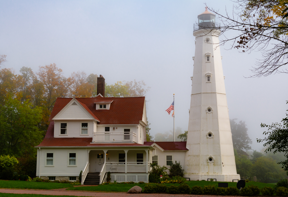The "North Point Lighthouse" as the sun breaks through the morning fog. The white tower is attached to a white building with a red roof. 