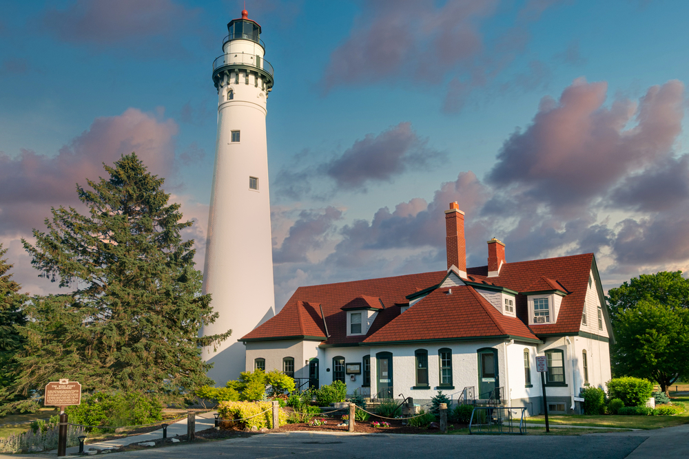 The Windpoint Lighthouse on Lake Michigan at dusk. The large white tower is next to a white building with a red roof. It's one of the best lighthouses in Wisconsin.  