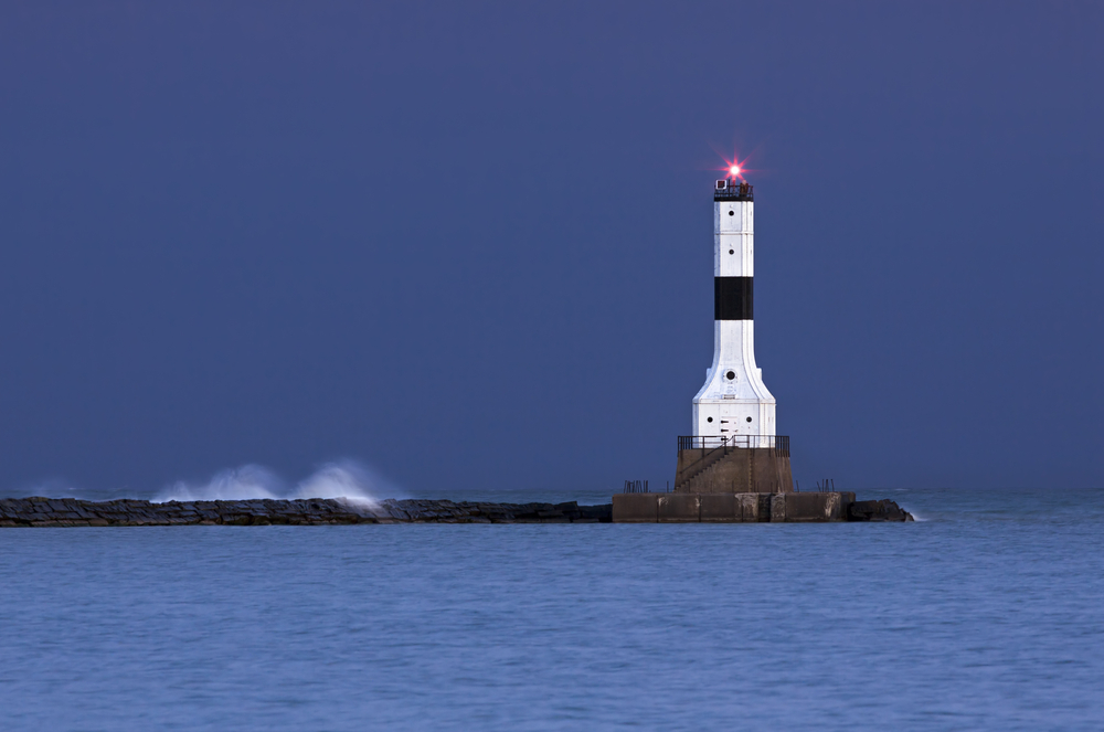 The white and black lighthouse  that is wider at the bottom then the top. It is at the end of the breakwater and the red light on the top is shining. 