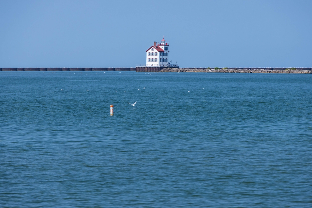 A white square ligthhouse with a red roof on the breakwater. The sea is in the foreground.  