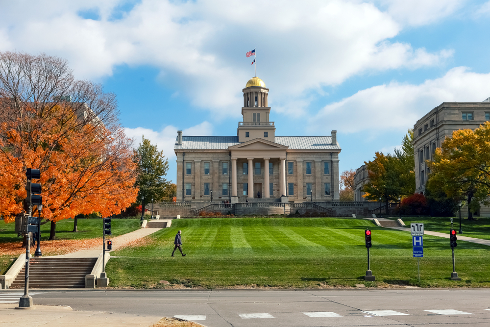 The view of the Old Capitol Building from the street. It has a large green lawn in front of it, and you can see trees with orange, red, yellow, and green leaves. 