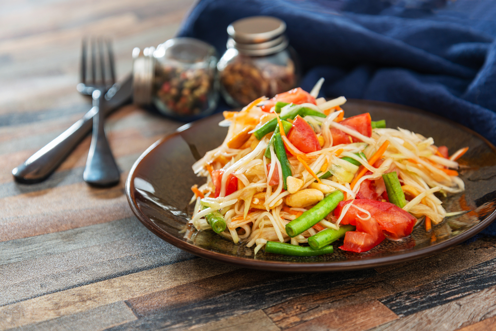 A plate of papaya salad that has peppers, beans, bean sprouts, nuts, and papaya. 