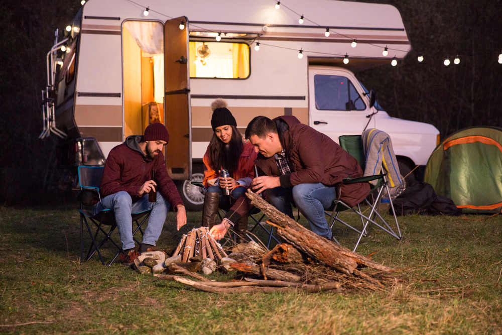 Three people sitting in front of an RV at a small bonfire at night. 