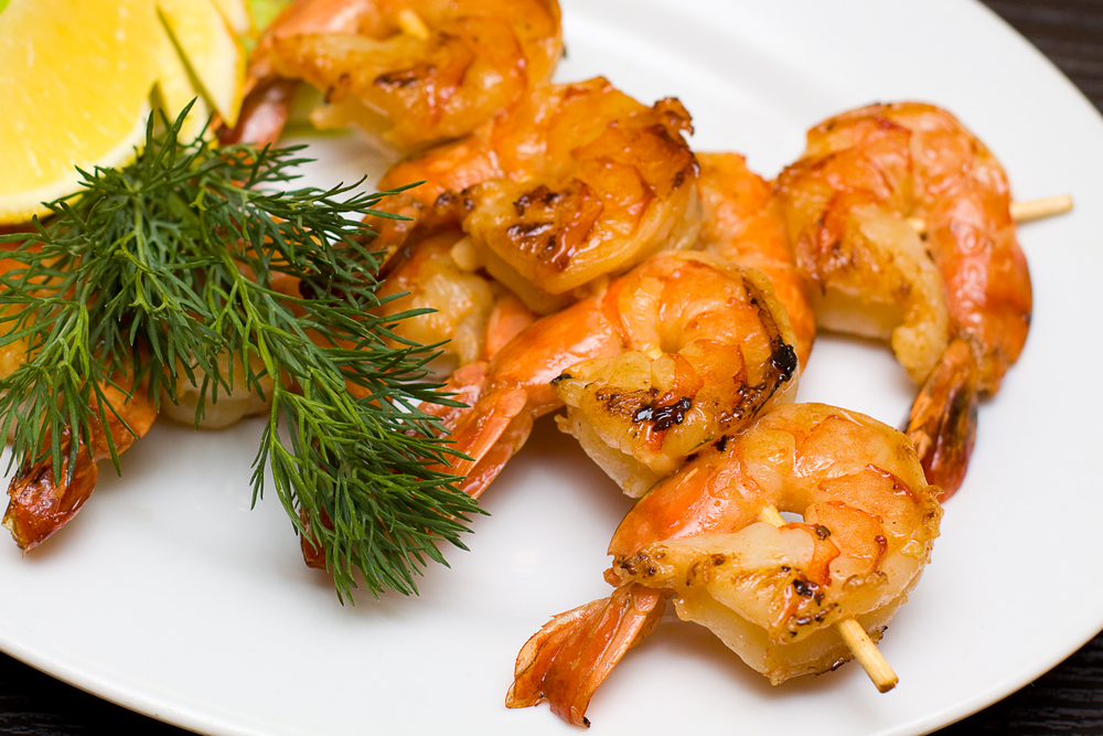 Grilled shrimp on a white plate with dill and lemon
