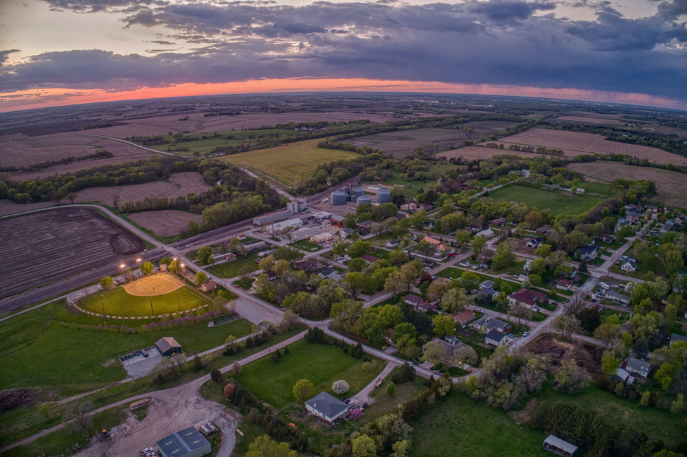 An aerial view of Nebraska as the sun is setting. You can see homes, other buildings, fields, and a large baseball diamond. 