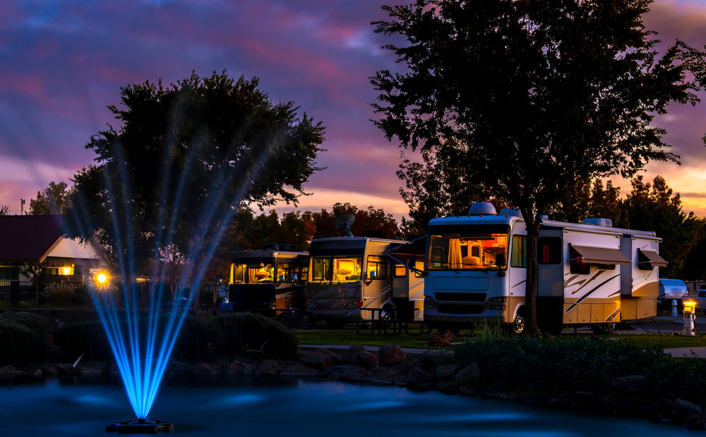 A luxury RV resort at night with a large fountain and rows of large RVs. 