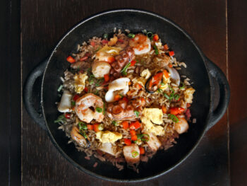A black bowl full of seafood rice, similar to what you'll find at restaurants in Dayton. The rice has shrimp, calamari, octopus, fried eggs, vegetables, and rice.