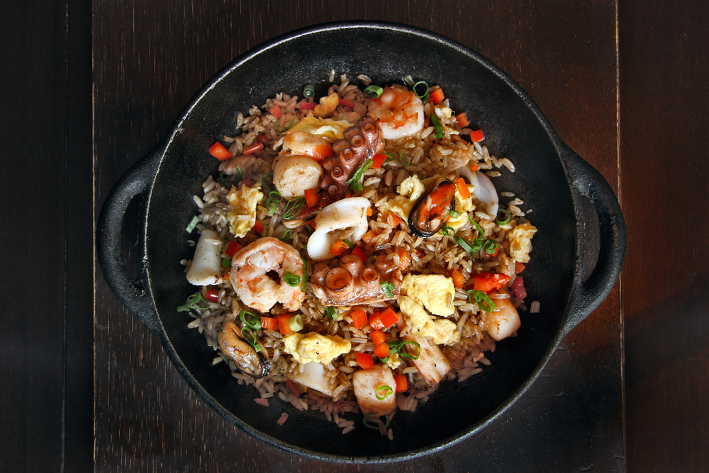 A black bowl full of seafood rice, similar to what you'll find at restaurants in Dayton. The rice has shrimp, calamari, octopus, fried eggs, vegetables, and rice. 
