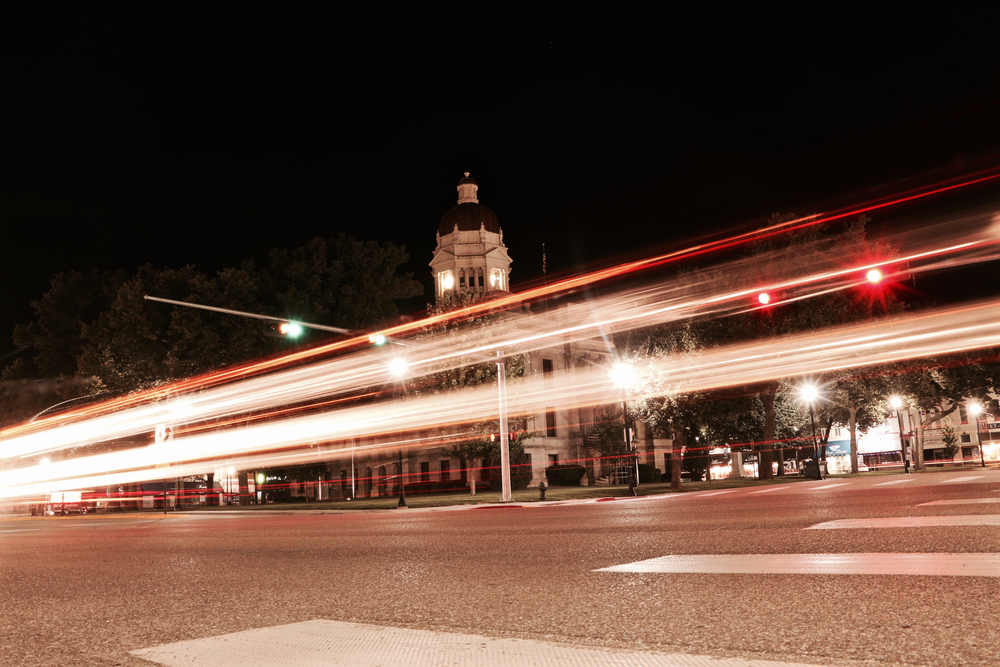 The main street of Seward, a small town in Nebraska, at night. You can see a historic building and light trails form where cars have driven by. 