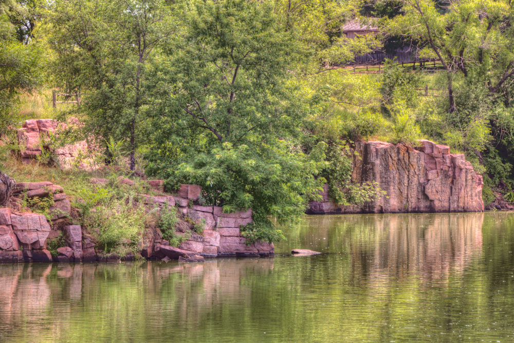 Lake in Arrowhead Park with rocky bluffs and green trees.